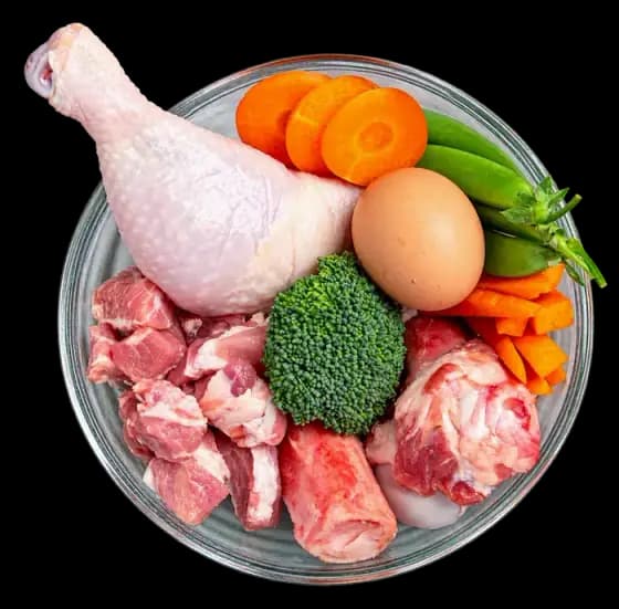 Semangkuk daging ayam mentah, telur, brokoli, dan wortel
